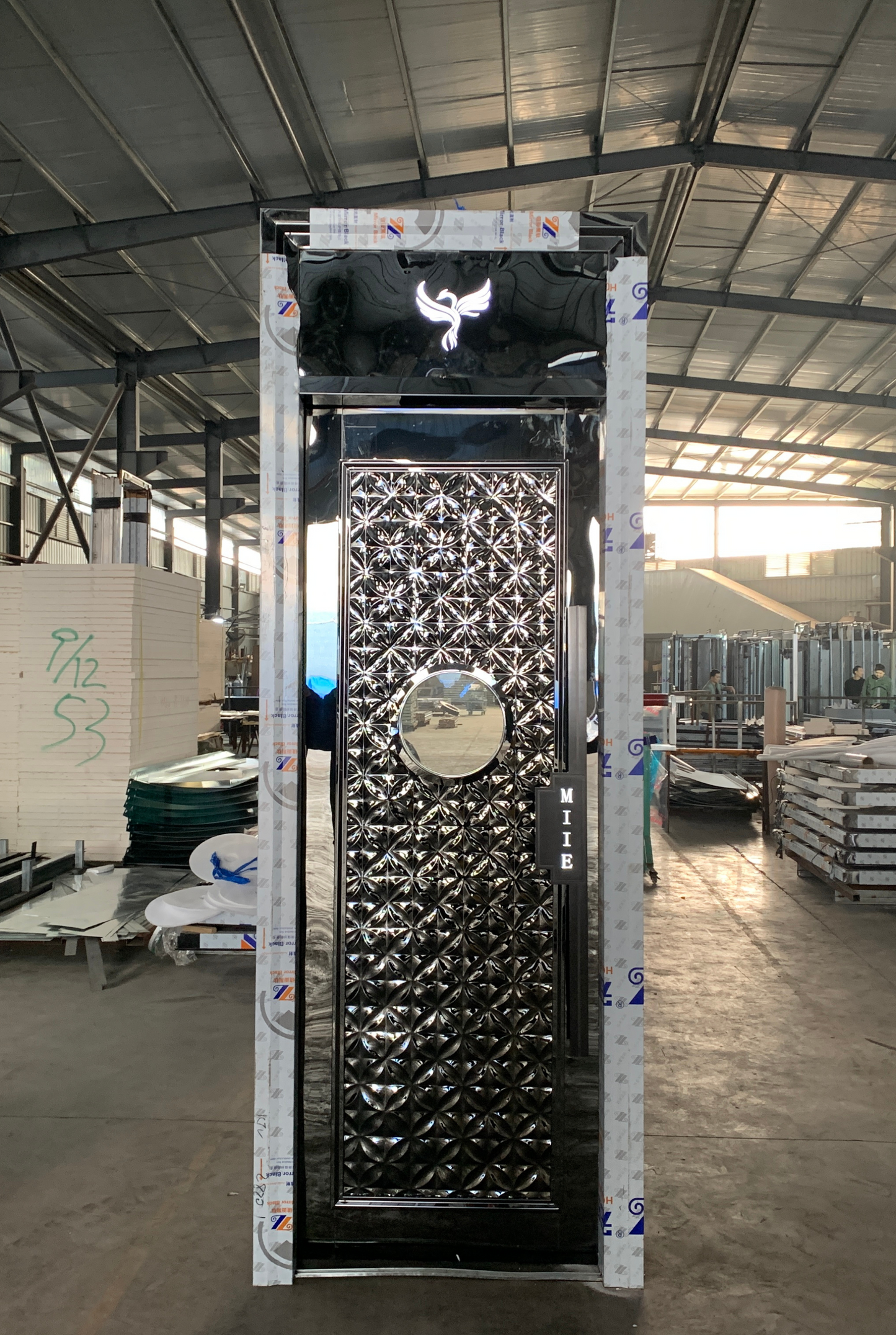 Black stainless steel soundproof door with embossed floral panel and a round window, suitable for luxurious KTV or entertainment room designs.