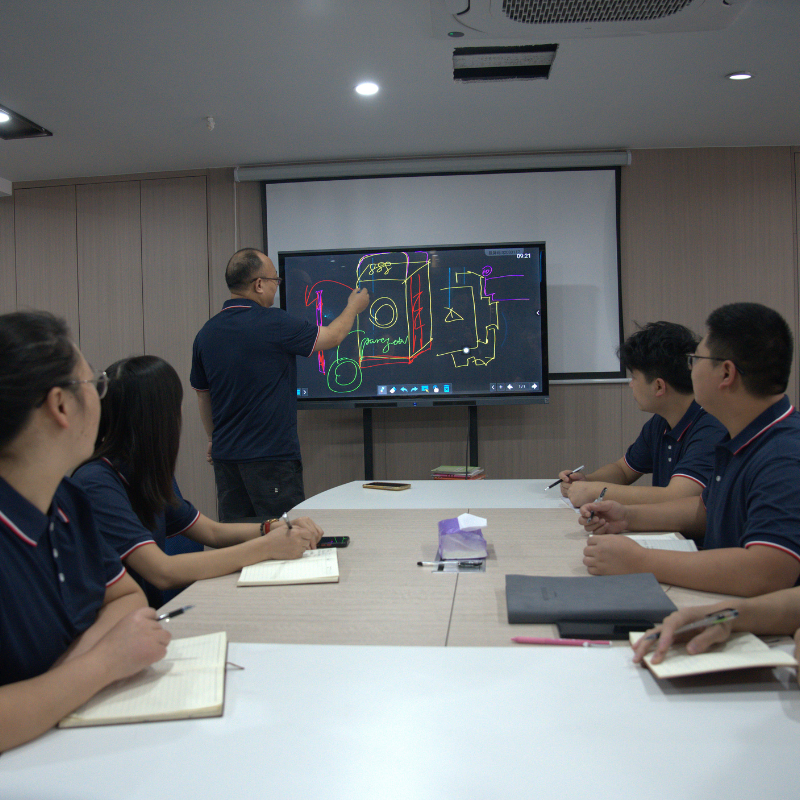Team members engaged in a discussion during a meeting, reviewing technical drawings on a digital whiteboard, focusing on soundproof door design.