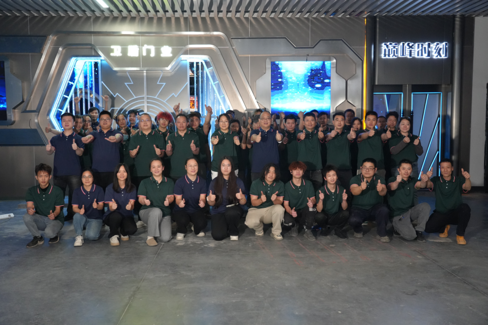 Group photo of the team at a company event, posing with thumbs up in front of the company logo and futuristic decor.